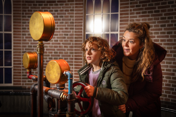 Moeder en zoon draaien aan de raders van de stoommachine in attractie De Waterwolf