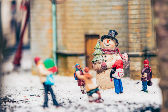 Madurodammertjes in de sneeuw in winters Madurodam: een man tilt kerstinkopen, ouder en kind bewonderen een sneeuwpop