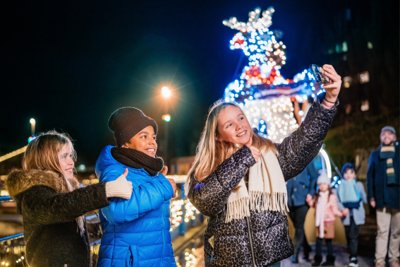 3 Kinderen maken samen een selfie maken in winters Madurodam, verlichting op de achtergrond