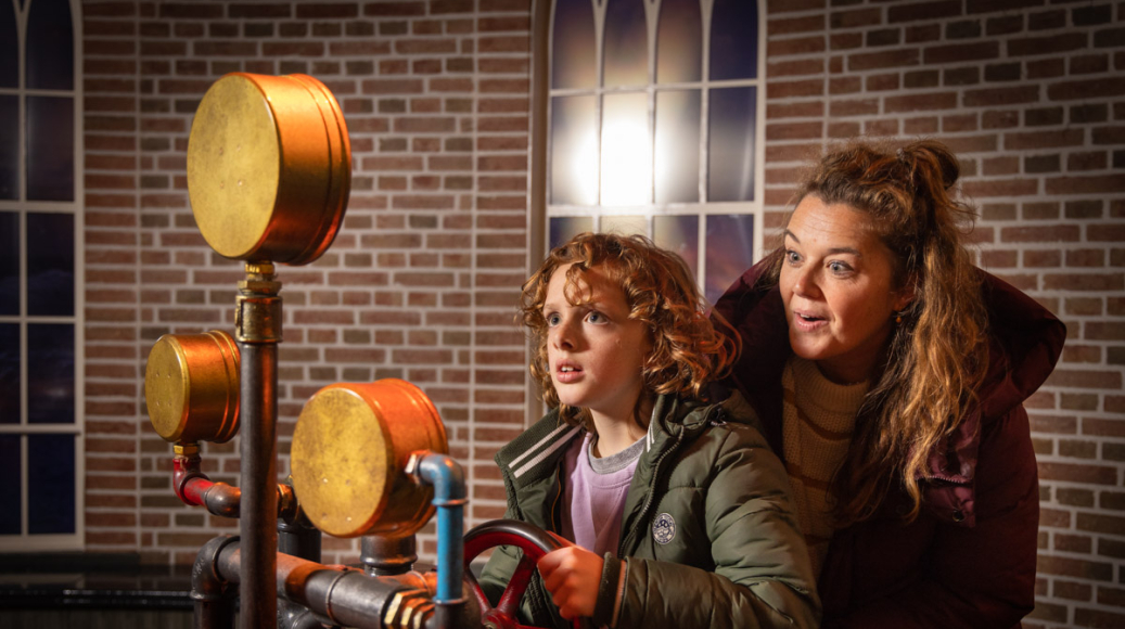 Moeder en zoon draaien aan de raders van de stoommachine in attractie De Waterwolf