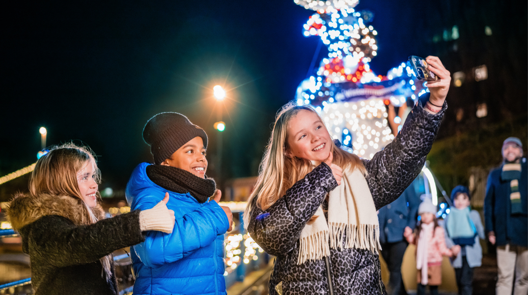 3 Kinderen maken samen een selfie maken in winters Madurodam, verlichting op de achtergrond